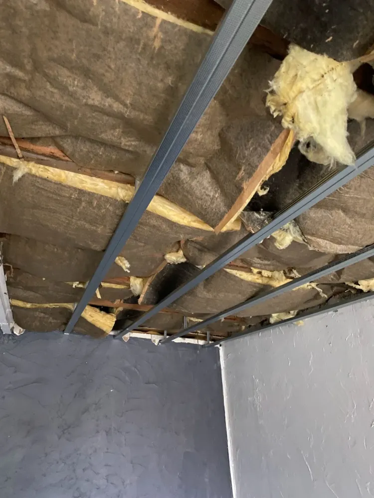 Détail de l'ossature métallique et de l'isolation d'un plafond en rénovation, au-dessus d'un mur peint en gris anthracite