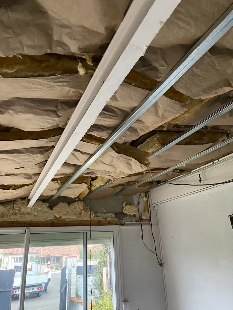 Installation de rouleaux d'isolation en laine de verre entre les solives en bois, maintenus par la nouvelle structure métallique