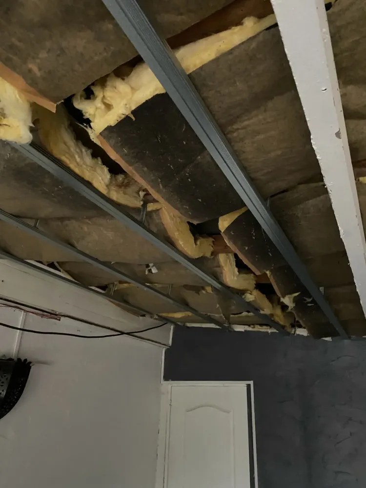 Vue intérieure montrant l'installation d'une ossature métallique pour un plafond suspendu sous une ancienne charpente en bois