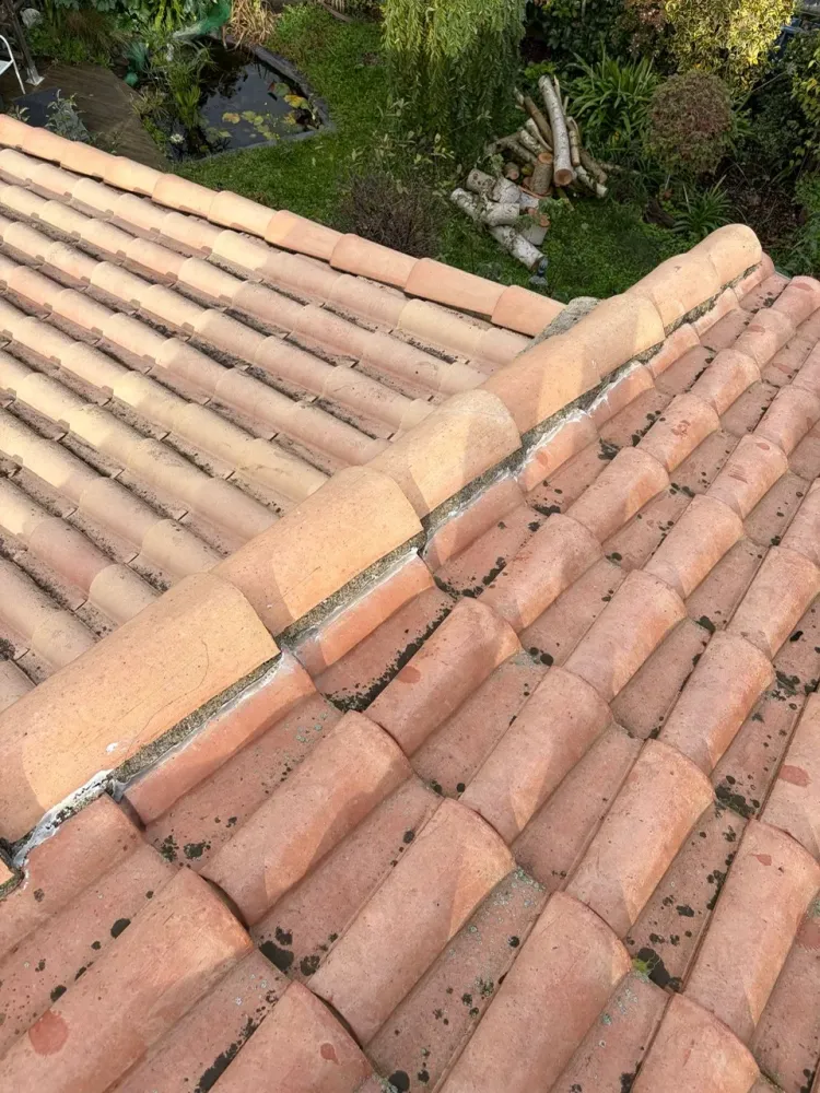 Gros plan sur la crête du toit montrant les tuiles faîtières scellées au mortier avec des éclats de mortier sec et des débris à nettoyer