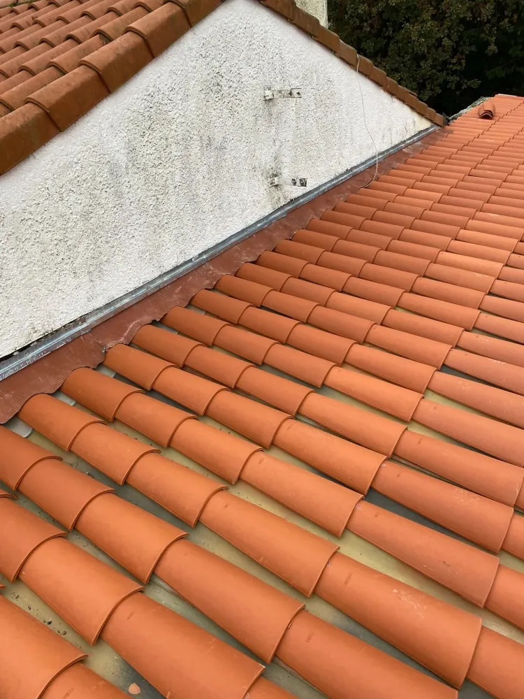 Détail de l'étanchéité entre une toiture en tuiles romanes neuves et un mur de façade avec une bande de plomb et un solin métallique