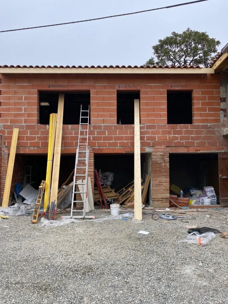 Une maison en construction avec des briques et du bois, montrant les fondations et la structure en cours d'assemblage